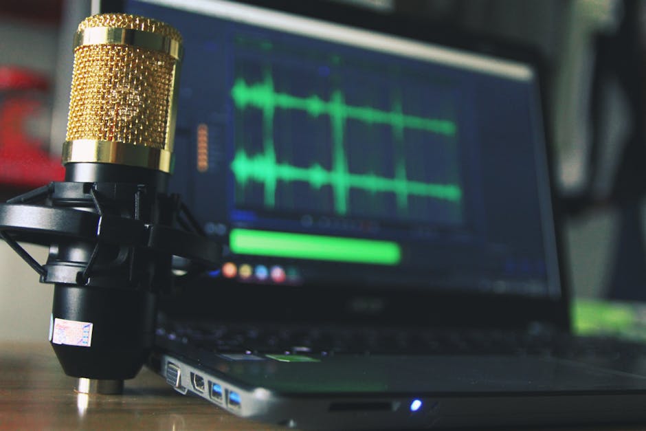 Close-up of a golden microphone and laptop used for audio editing.